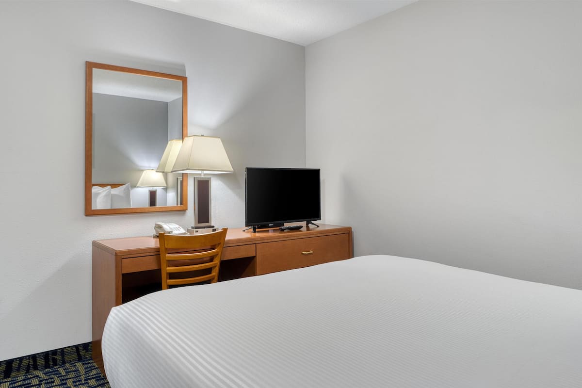 A hotel room with a bed, a desk with a lamp, a television, and a mirror.