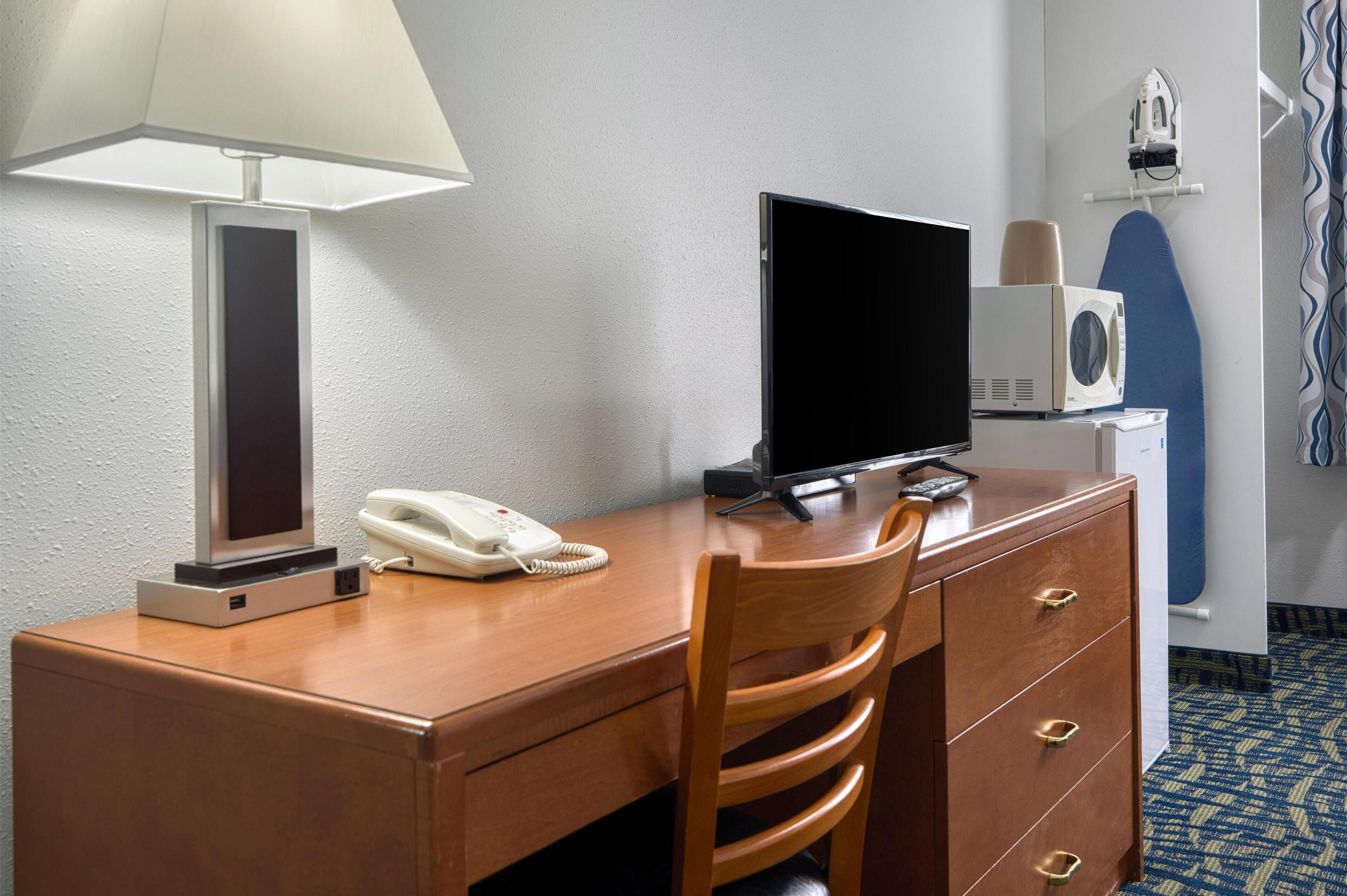 Une chambre d’hôtel équipée d’un bureau en bois, d’une lampe, d’un téléphone, d’une télévision, d’une planche à repasser et d’un fer à repasser.