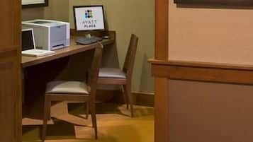 Quarto de hotel com escrivaninha, impressora, monitor de computador e cadeira.