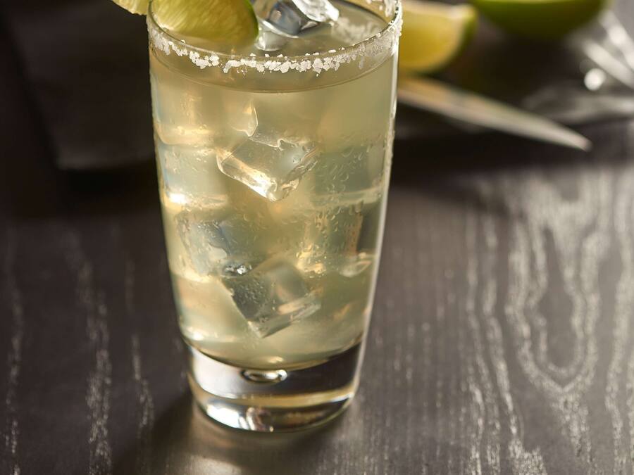 Un verre contenant une boisson claire, avec des glaçons et une tranche de citron vert, posé sur une table en bois sombre.
