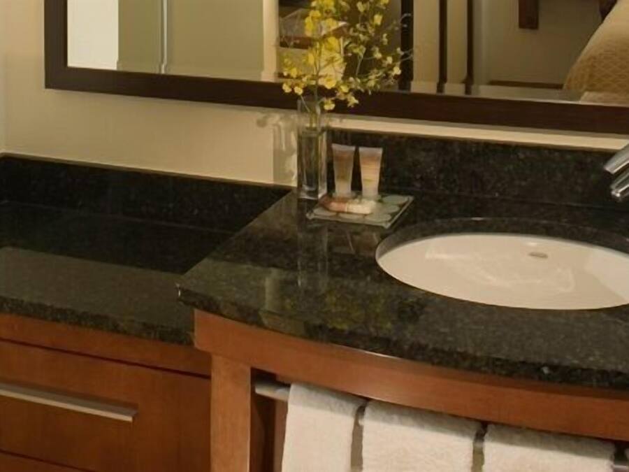 A bathroom with a black granite countertop, a white sink, a mirror, and a wooden cabinet with a drawer.