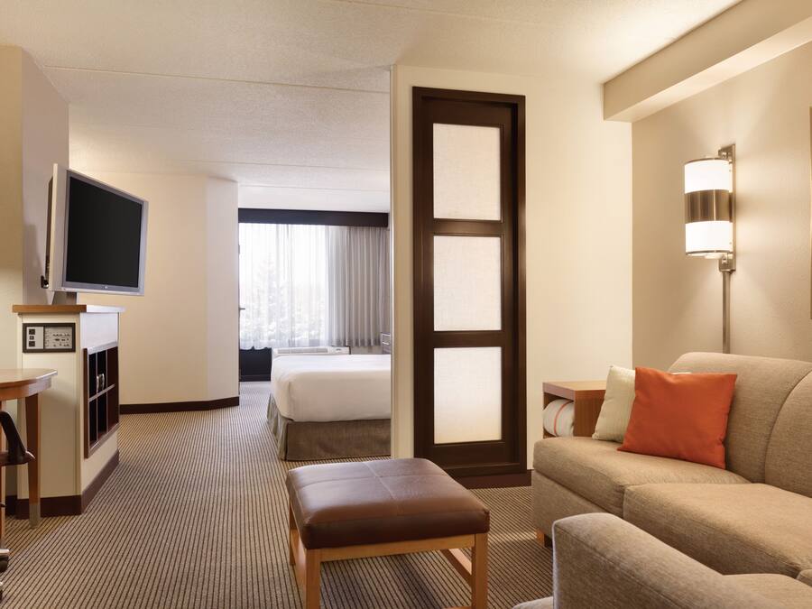 A hotel room with a bed, a TV, a desk, a couch, and a painting on the wall.