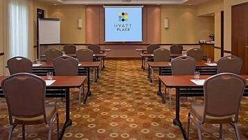 A conference room with a carpeted floor, multiple tables, and chairs arranged for meetings. A projector screen displays the Hyatt Place logo.