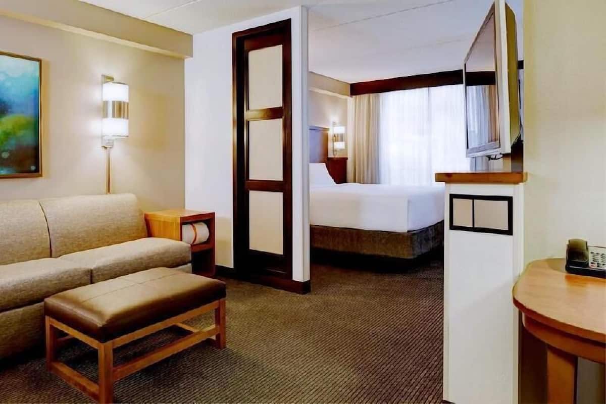 Habitación de hotel con cama, sofá, una mesita, televisión y una puerta que da a otra habitación.
