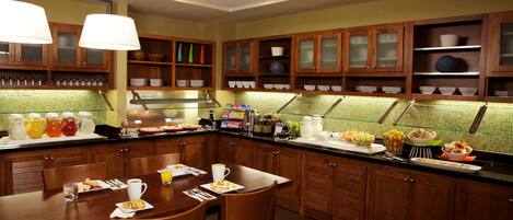 Una cocina de hotel con armarios de madera, una barra de desayuno y diferentes alimentos para el desayuno a la vista.