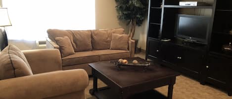 Una sala de estar con un sofá color beige, una mesa de centro de madera oscura y un televisor sobre un mueble negro.
