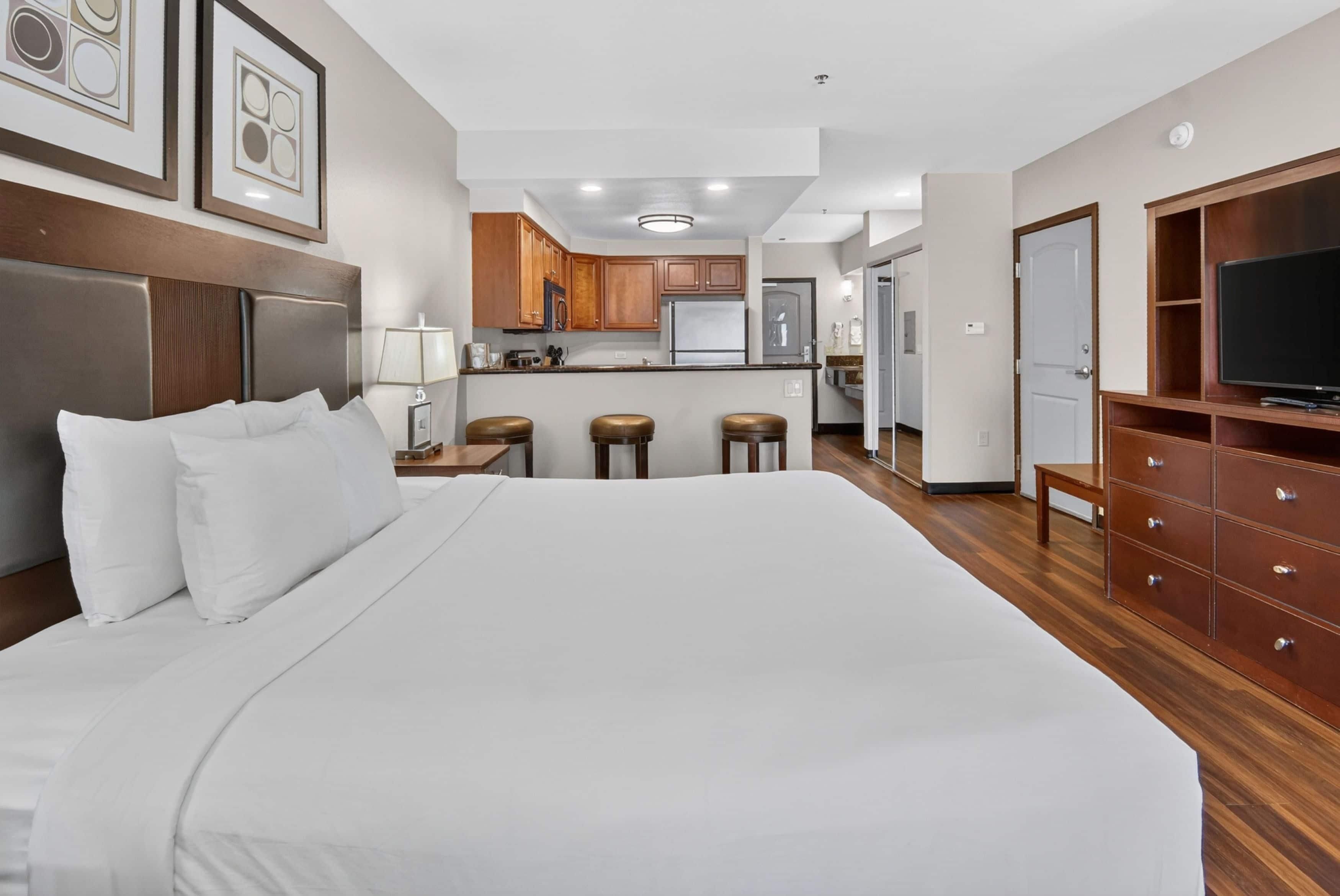A hotel room with a large bed, a kitchenette, a TV, and a wooden dresser.