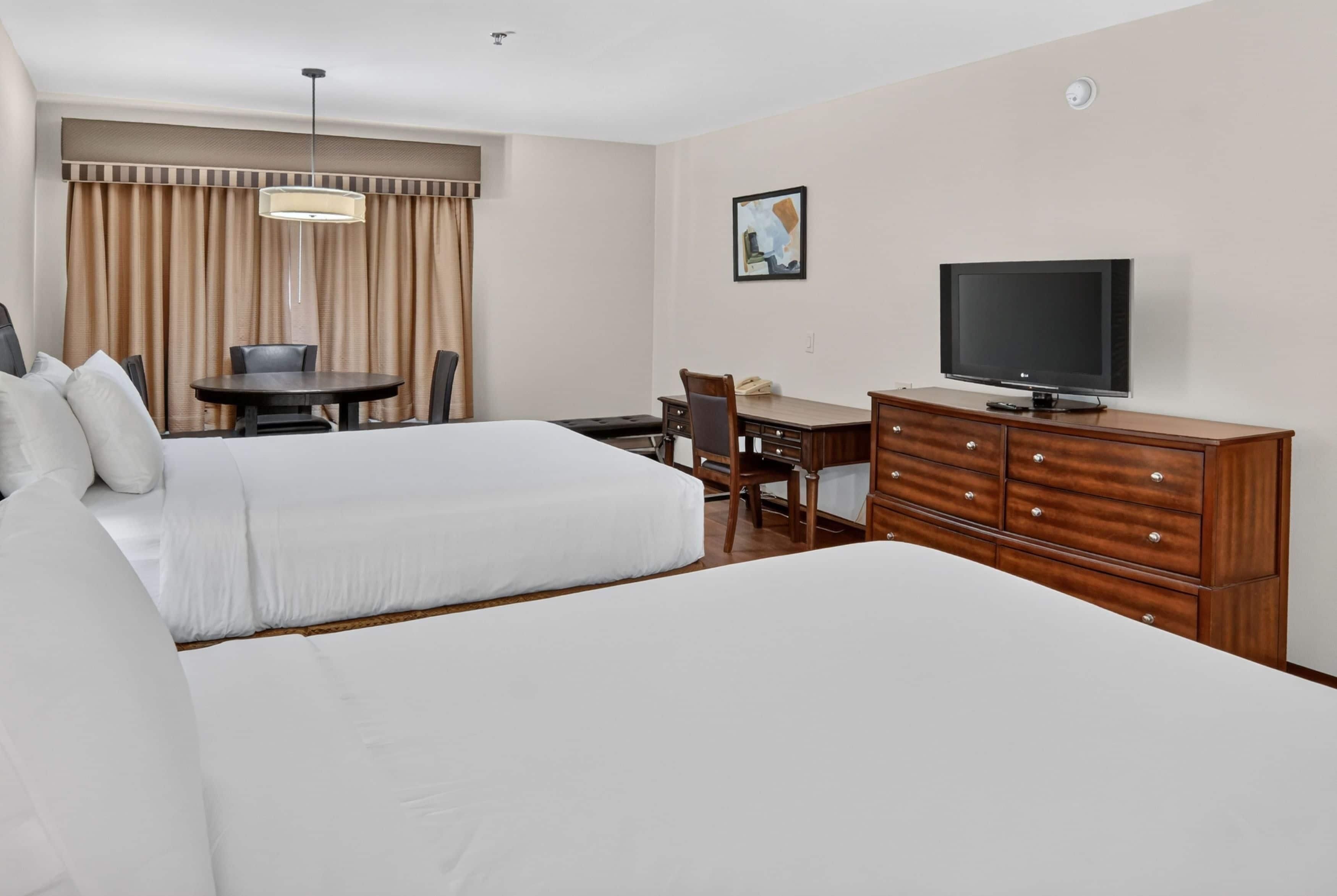 Een hotelkamer met twee bedden, een bureau, een stoel, een televisie en een raam met gordijnen.