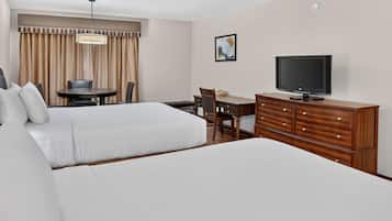 A hotel room with two beds, a desk, a chair, a television, and a window with curtains.