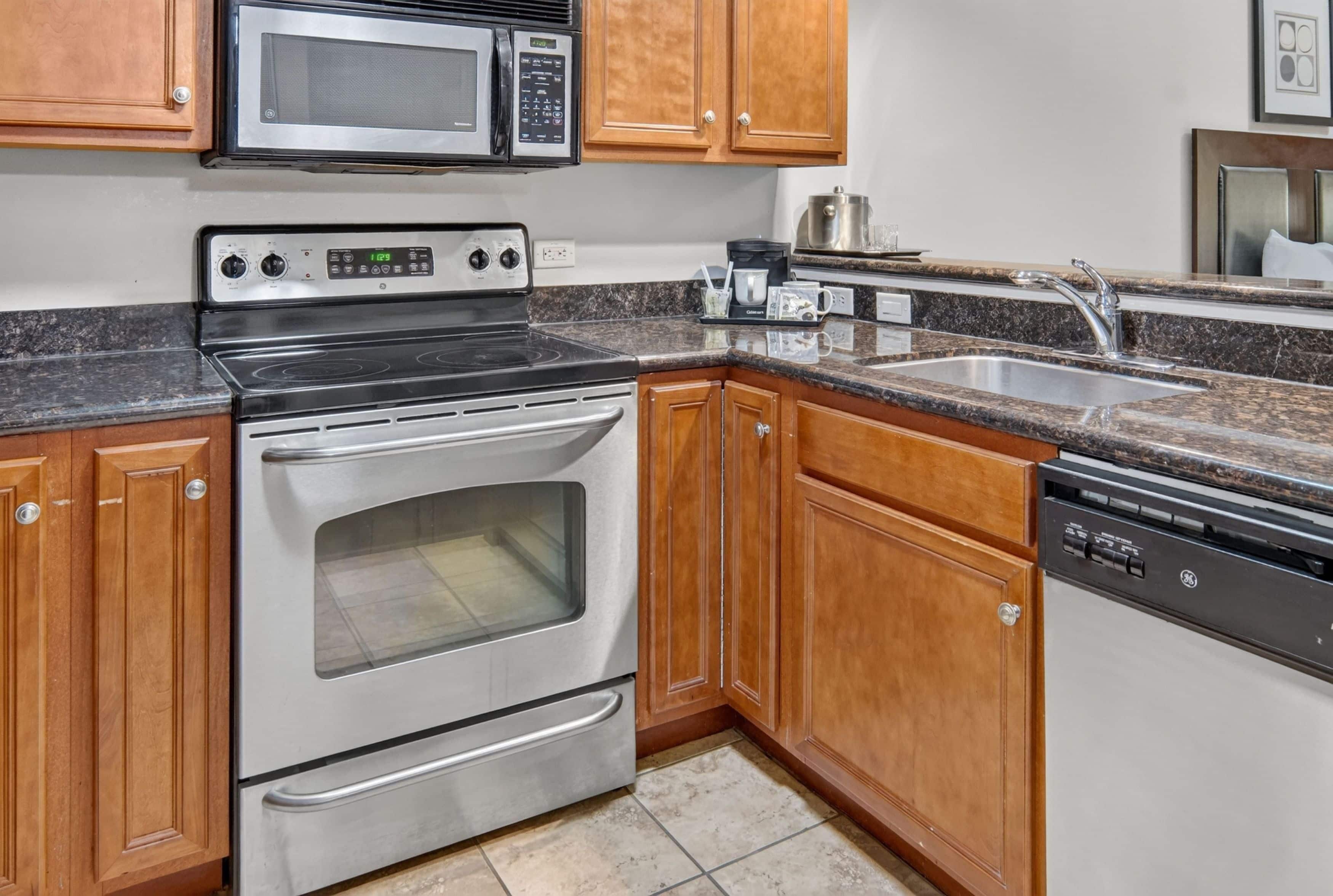 A kitchen with stainless steel appliances, wooden cabinets, a granite countertop, and a built-in dishwasher.