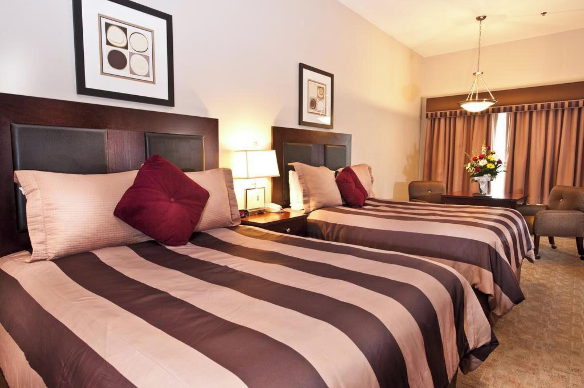 A hotel room with two beds, a desk, a chair, and a window with curtains.
