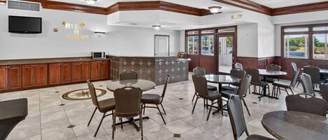 A spacious indoor dining area with multiple tables and chairs, a kitchen area with a microwave, and a television mounted on the wall.