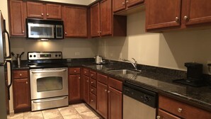 A kitchen with wooden cabinets, stainless steel appliances, a dishwasher, and a granite countertop. - Hawthorn Extended Stay by Wyndham Killeen (Killeen)