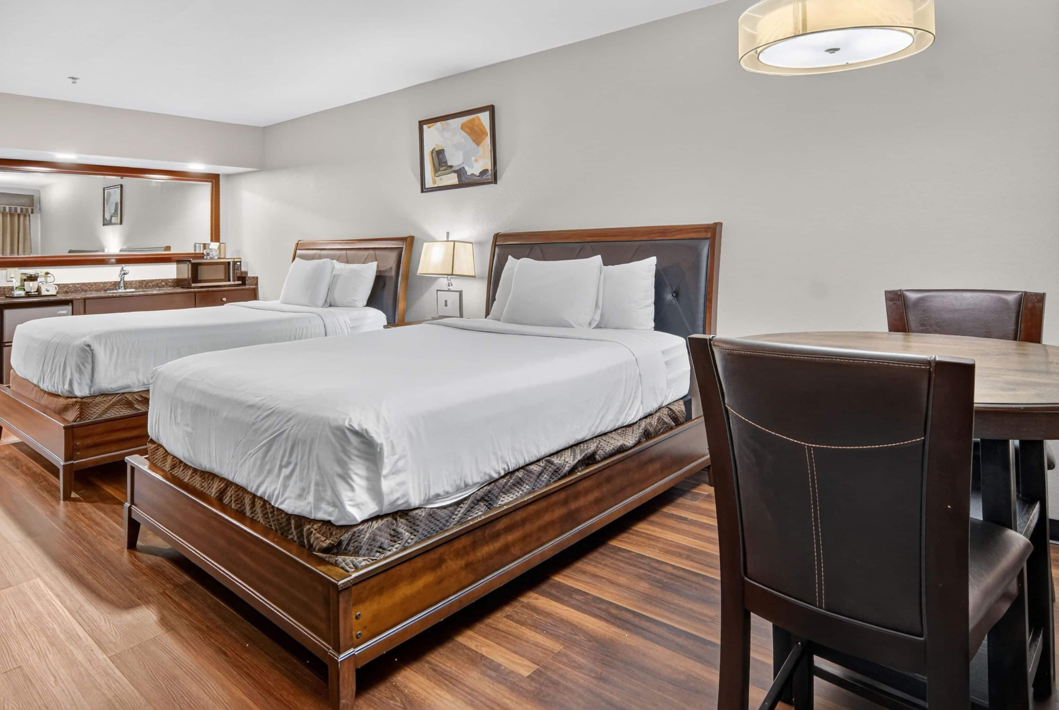 A hotel room with two beds, a dining table, and a chair.