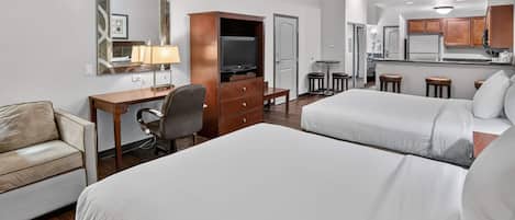 Habitación de hotel con dos camas, un escritorio, una silla, un televisor y una kitchenette.