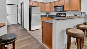 A kitchen with wooden cabinets, a stainless steel refrigerator, a microwave, and a stove. There are stools and a countertop.