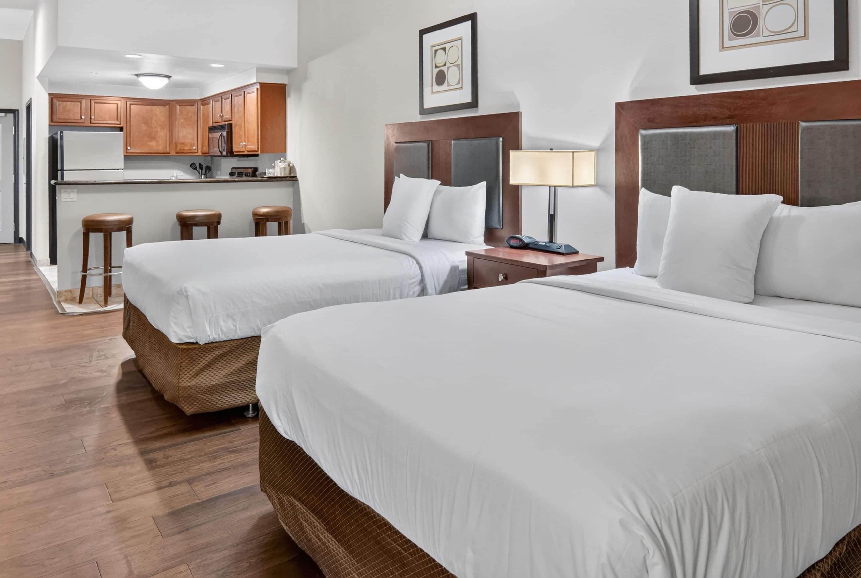 A hotel room with two beds, a kitchenette, and a bar area.