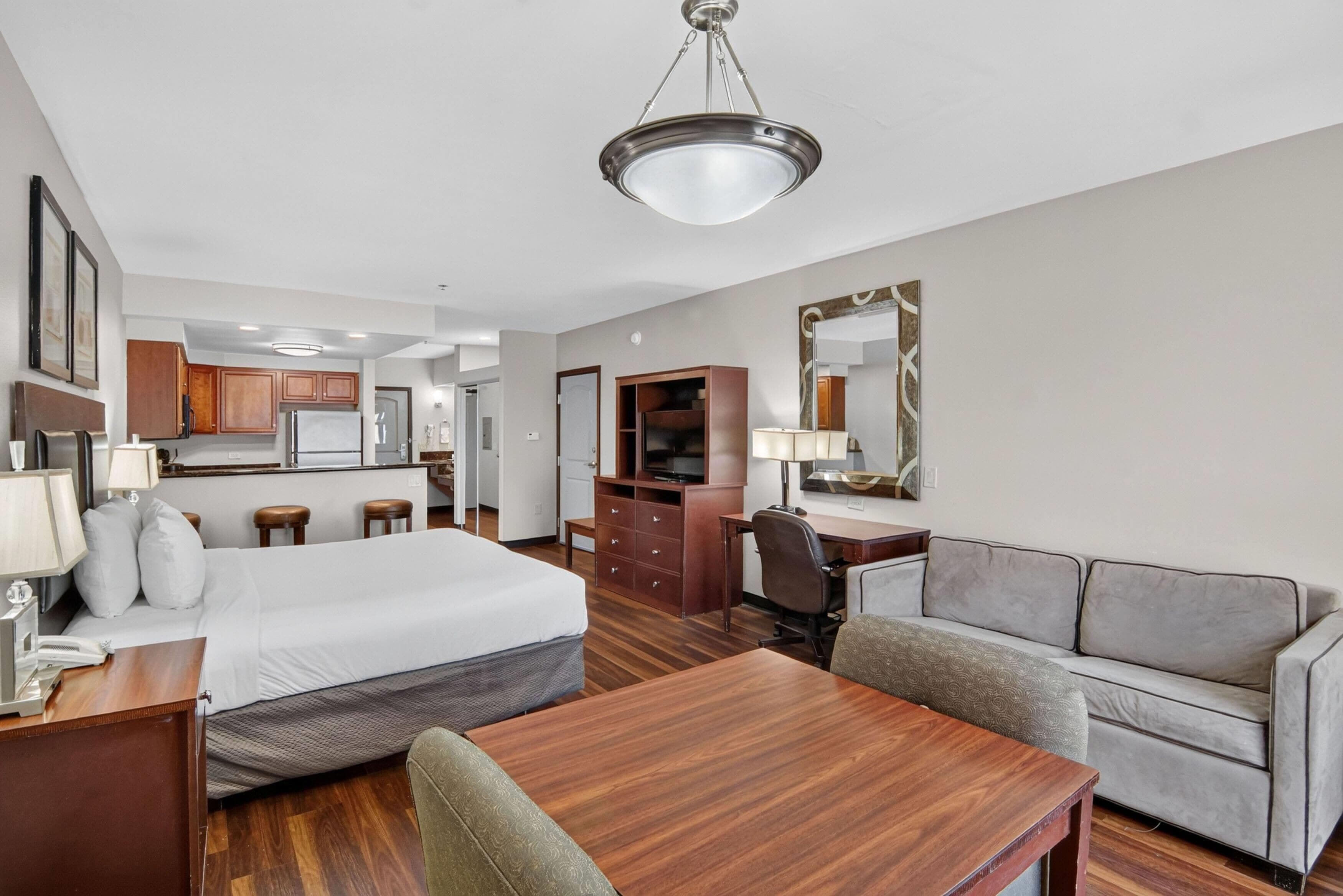 A hotel room with a bed, a desk, a chair, a sofa, a television, and a mirror.