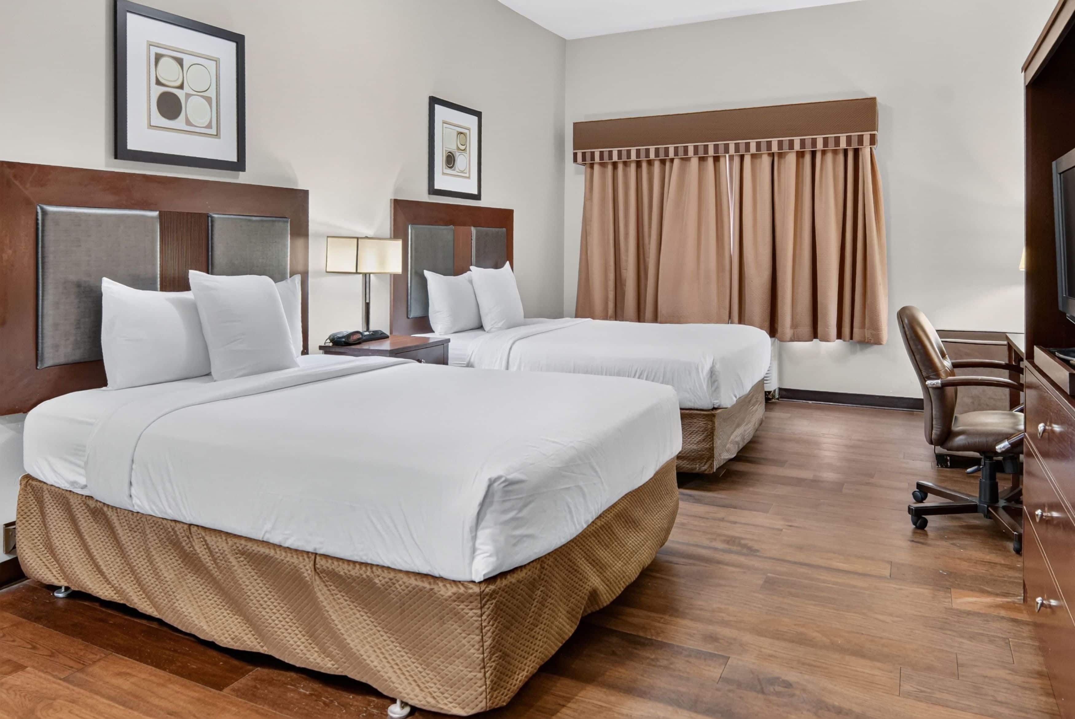 A hotel room with two beds, a desk, a chair, and a television.