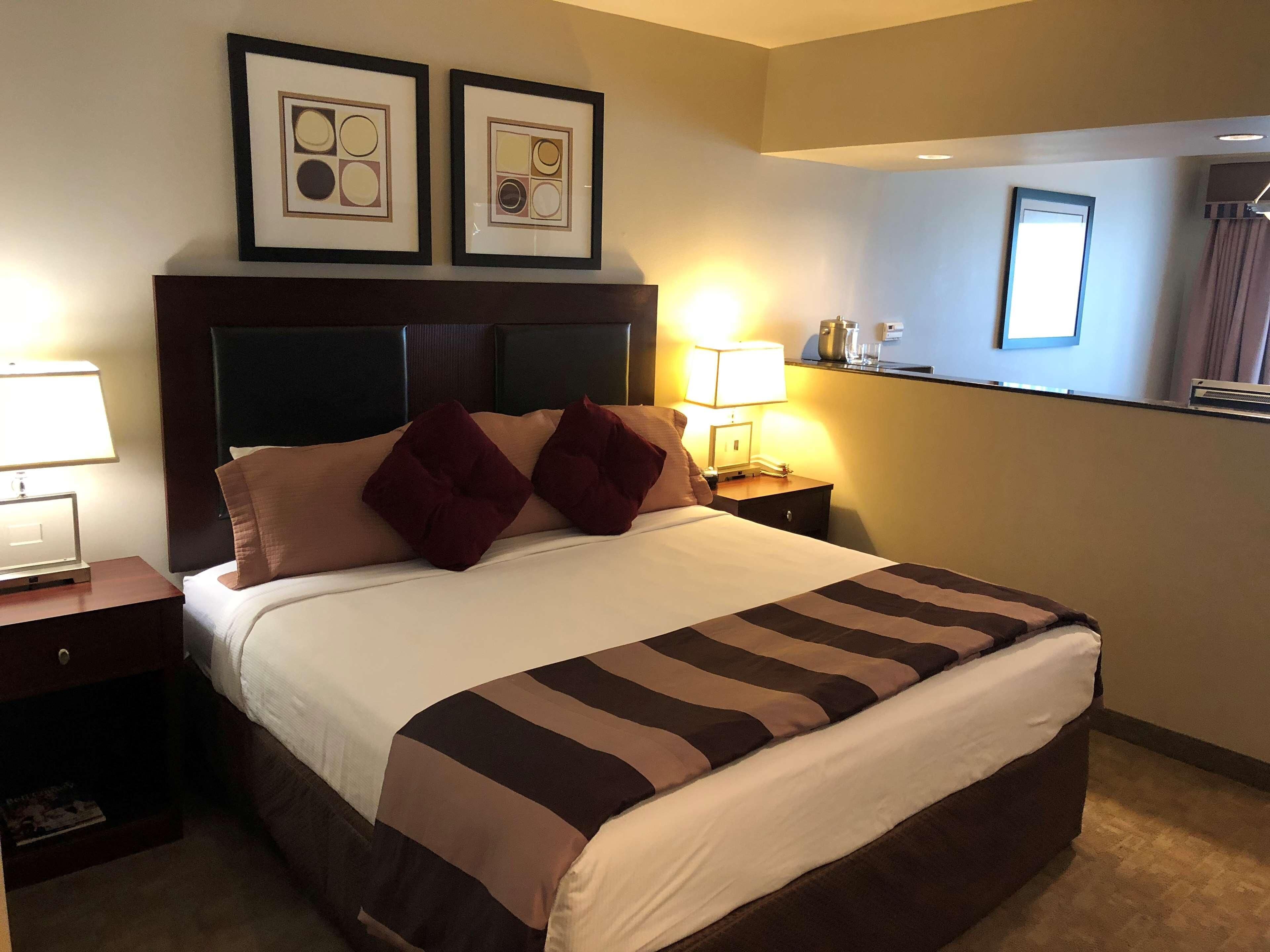 A hotel room with a large bed, two framed pictures on the wall, a bedside lamp, and a nightstand with a phone and a cup.
