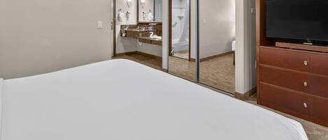 Habitación de hotel con una cama grande, un aparador de madera, un televisor y un baño con ducha y tocador.