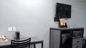Une chambre d’hôtel équipée d’un bureau, d’une chaise, d’une machine à café, d’une télévision, d’un four à micro-ondes et d’un petit placard.