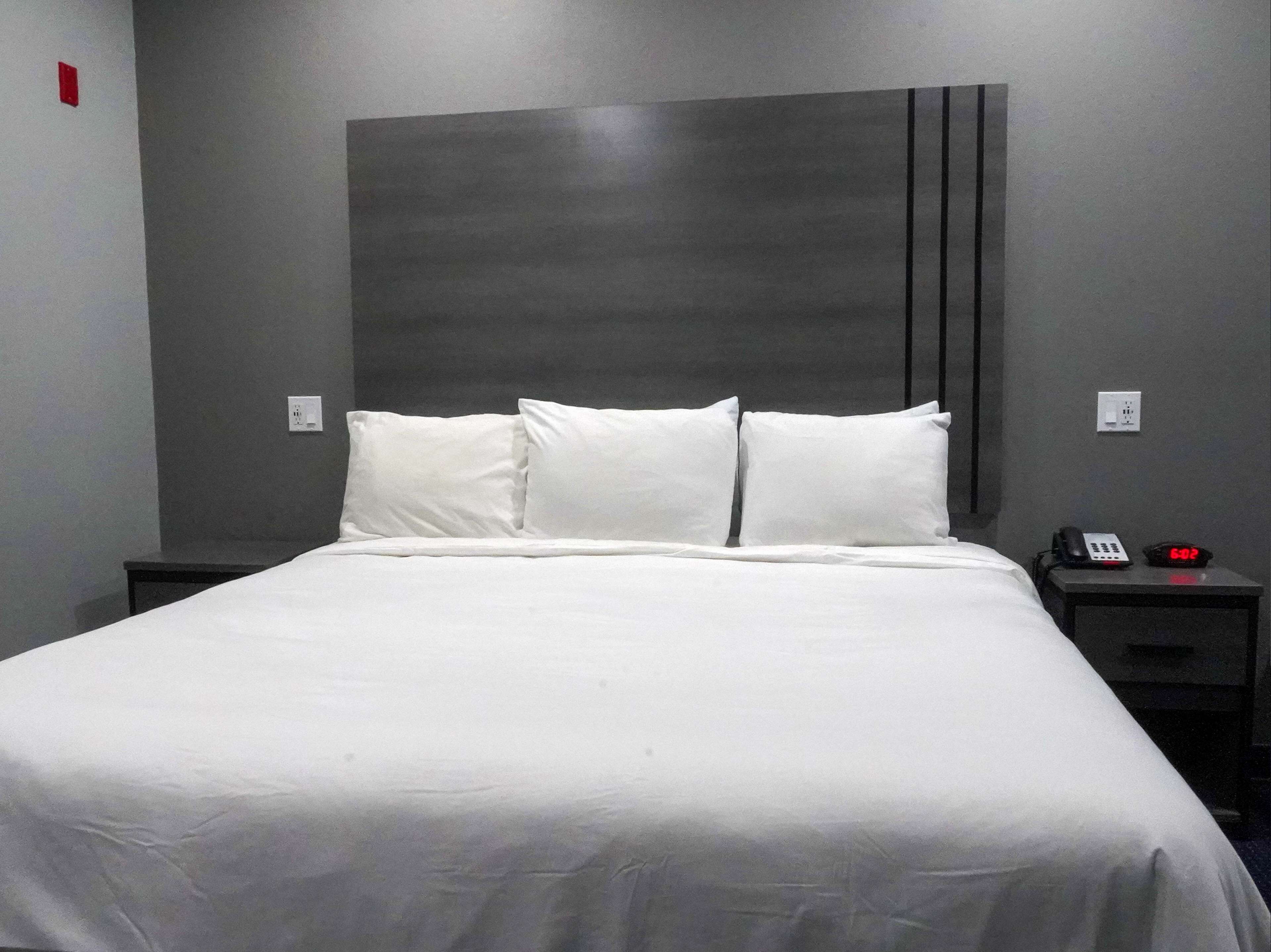 A neatly made bed with white linens and pillows, a modern headboard, and a bedside table with a phone and a clock.