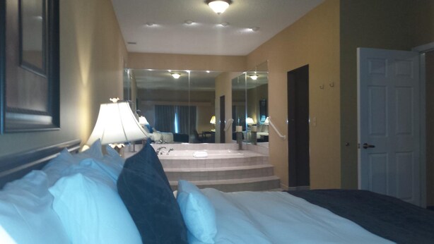 A hotel room with a bed, a lamp, a mirror, and a door. - Town & Country Inn and Suites (Quincy)