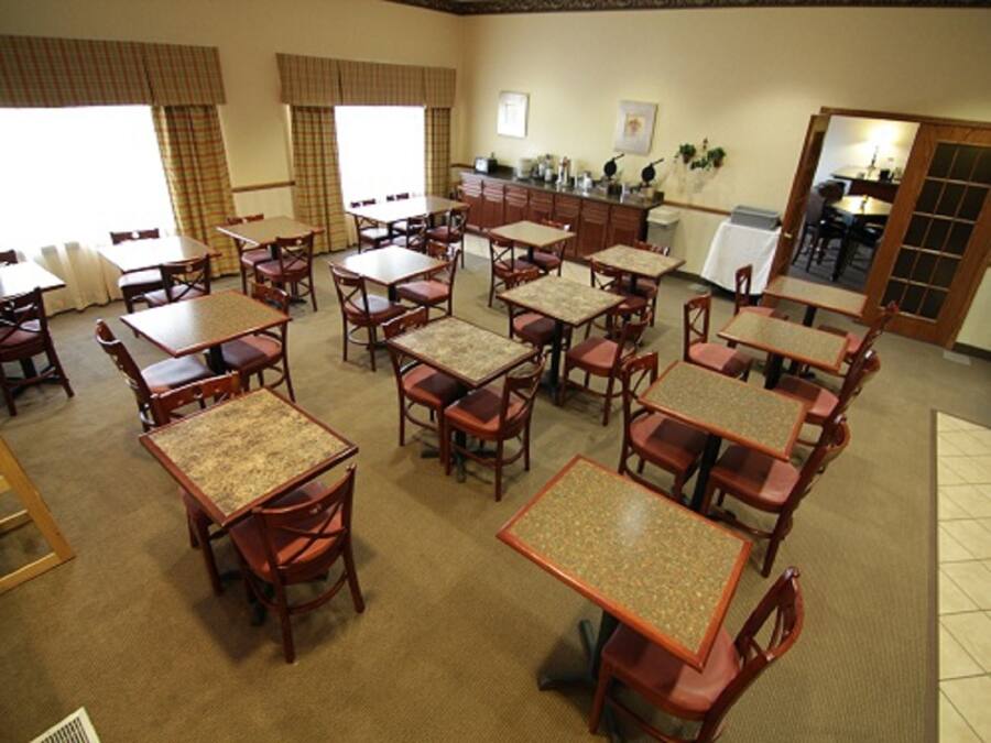 A dining area with multiple tables and chairs, a kitchen area, and large windows with curtains.