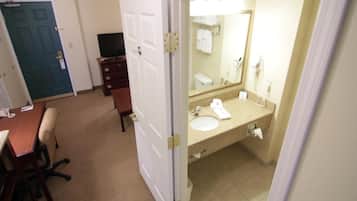 Une chambre d’hôtel équipée d’un bureau, d’une chaise, d’une commode et d’une salle de bain avec un lavabo, un miroir et un porte-serviettes.