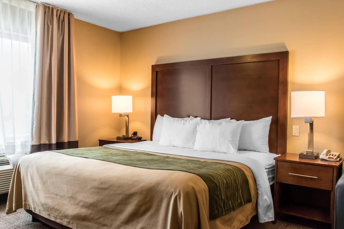 Habitación de hotel con una cama grande, dos lámparas de noche, una mesita de noche y una ventana con cortinas.