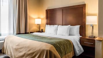 Una habitación de hotel con una cama, dos mesitas de noche, una lámpara y un ventanal con cortinas.