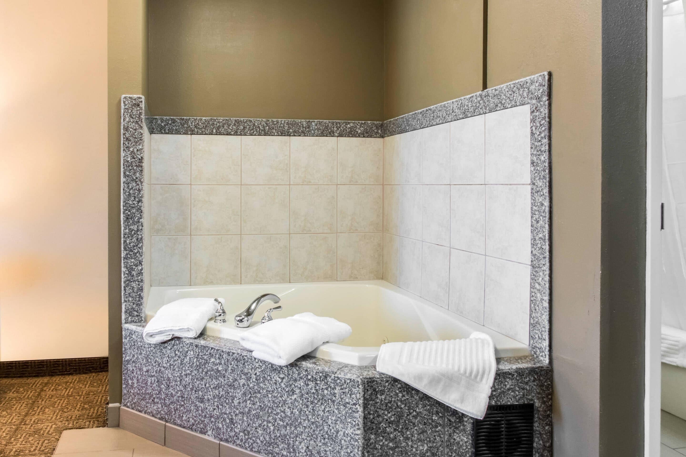 A corner bathroom with a granite countertop, a bathtub, and two white towels.