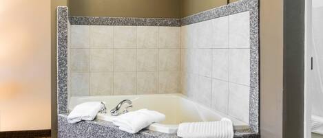 A corner bathroom with a granite countertop, a bathtub, and two white towels.