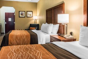 A hotel room with two beds, a desk with a telephone, a chair, and two wall-mounted lamps.
