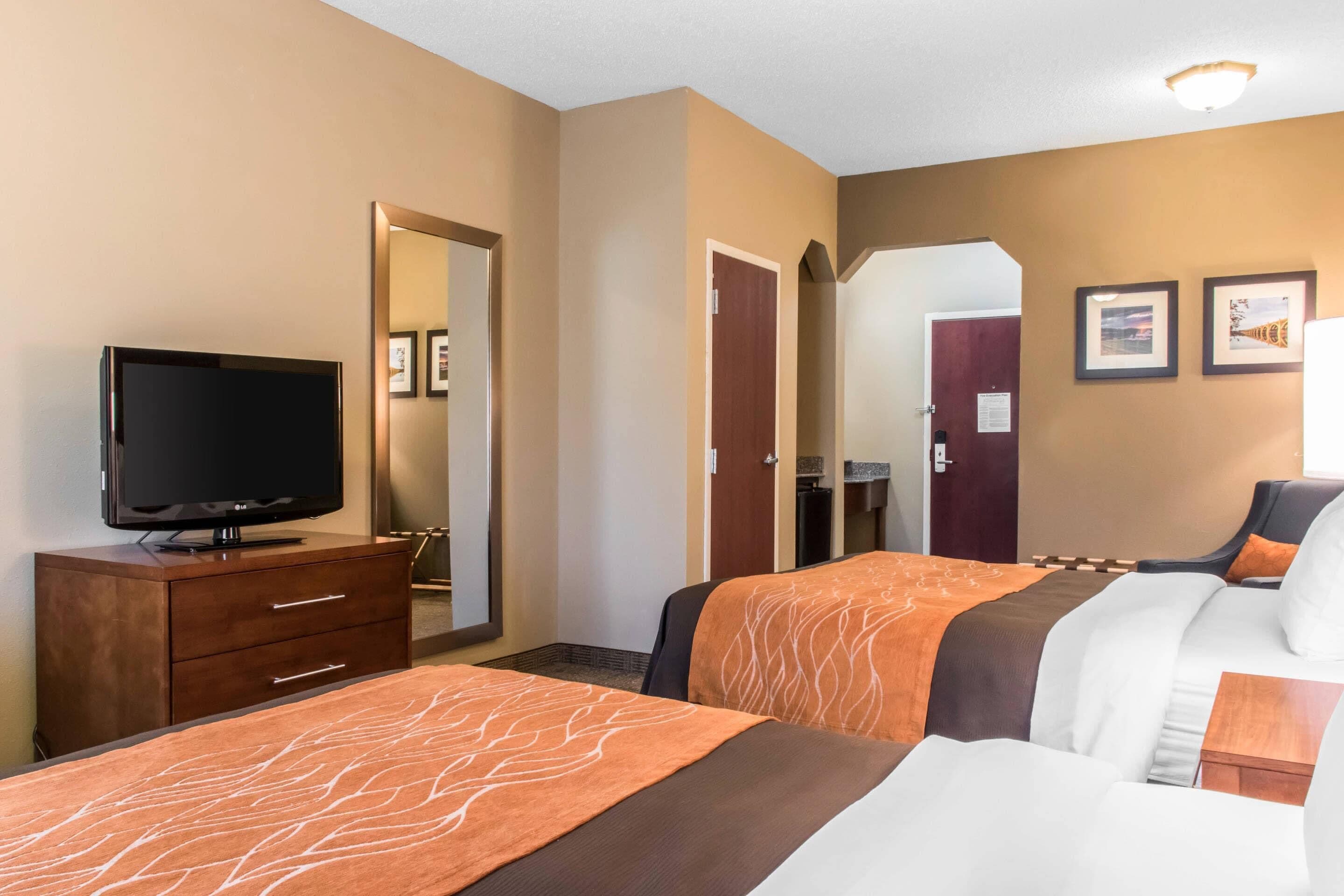 A hotel room with two beds, a TV on a dresser, and a door leading to a bathroom.