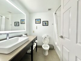 Un baño moderno con un lavamanos grande, inodoro y ducha. Hay cuadros enmarcados en la pared y un perchero para toallas.