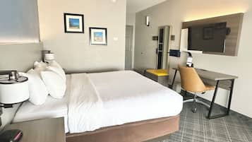 Une chambre d’hôtel avec un grand lit, un bureau avec une chaise, un téléviseur à écran plat et deux tableaux encadrés au mur.