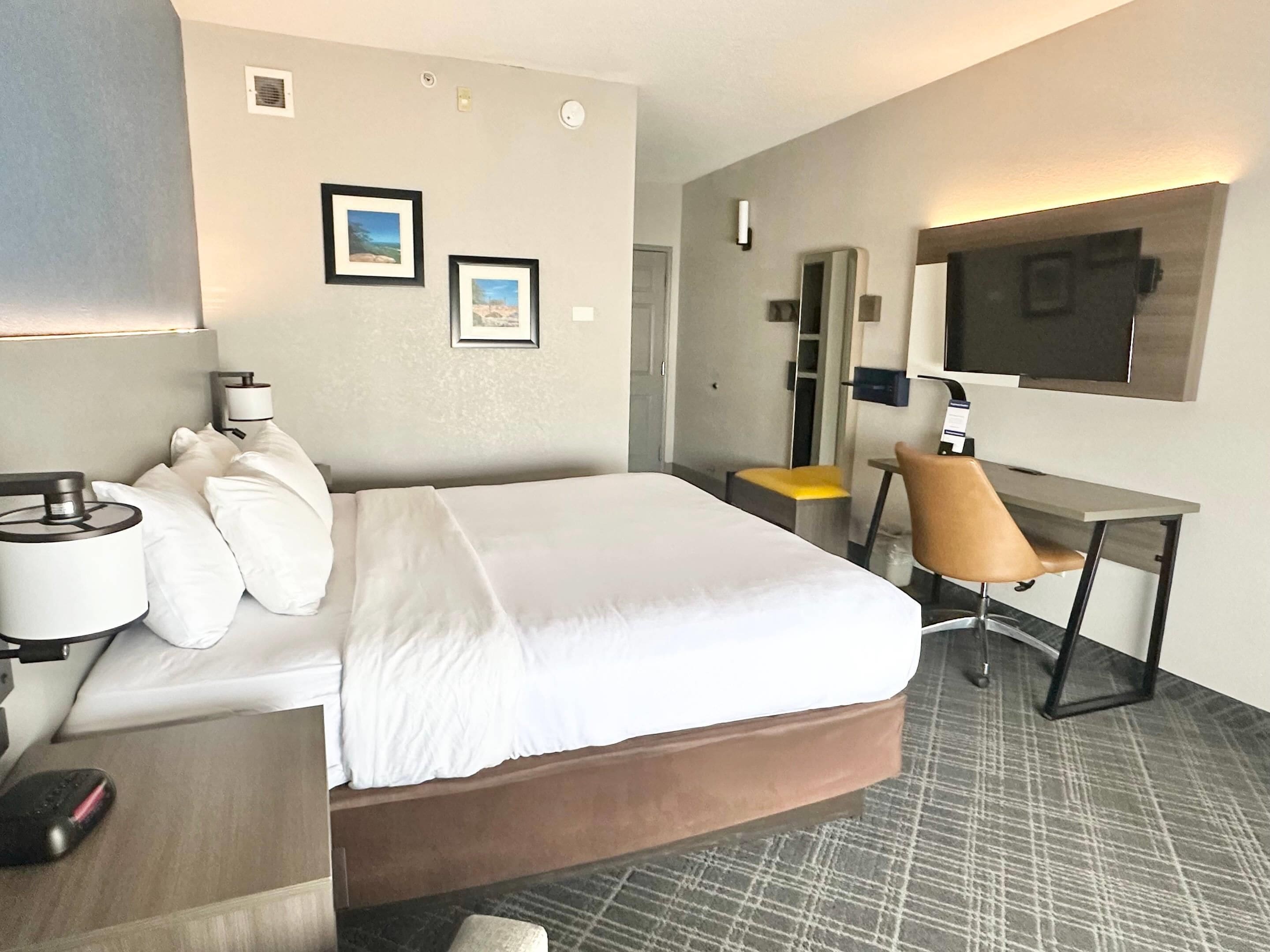 Habitación de hotel con cama, escritorio, silla, televisión y dos cuadros en la pared.