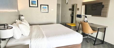Et hotelværelse med en seng, et skrivebord, en stol, et fjernsyn og to billeder hængende på væggen.