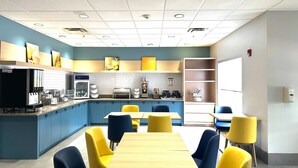 Een moderne keuken met blauwe kastjes, gele stoelen en een houten tafel.