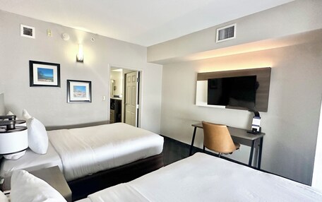 A hotel room with two beds, a desk, a chair, a TV, and framed pictures on the wall.