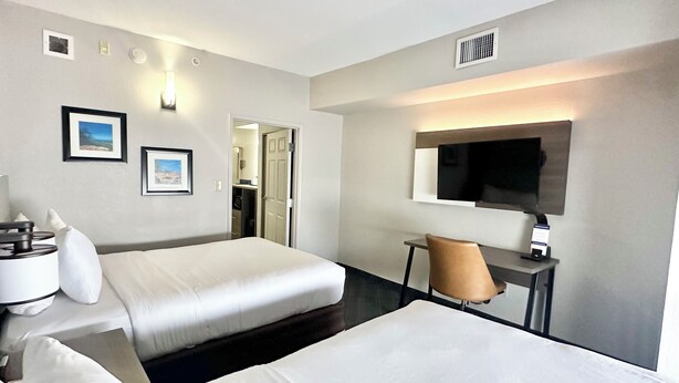 Een hotelkamer met twee bedden, een bureau, een stoel, een televisie en ingelijste foto’s aan de muur.