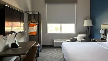 A hotel room with a bed, a desk, a chair, a TV, a window, and a lamp.