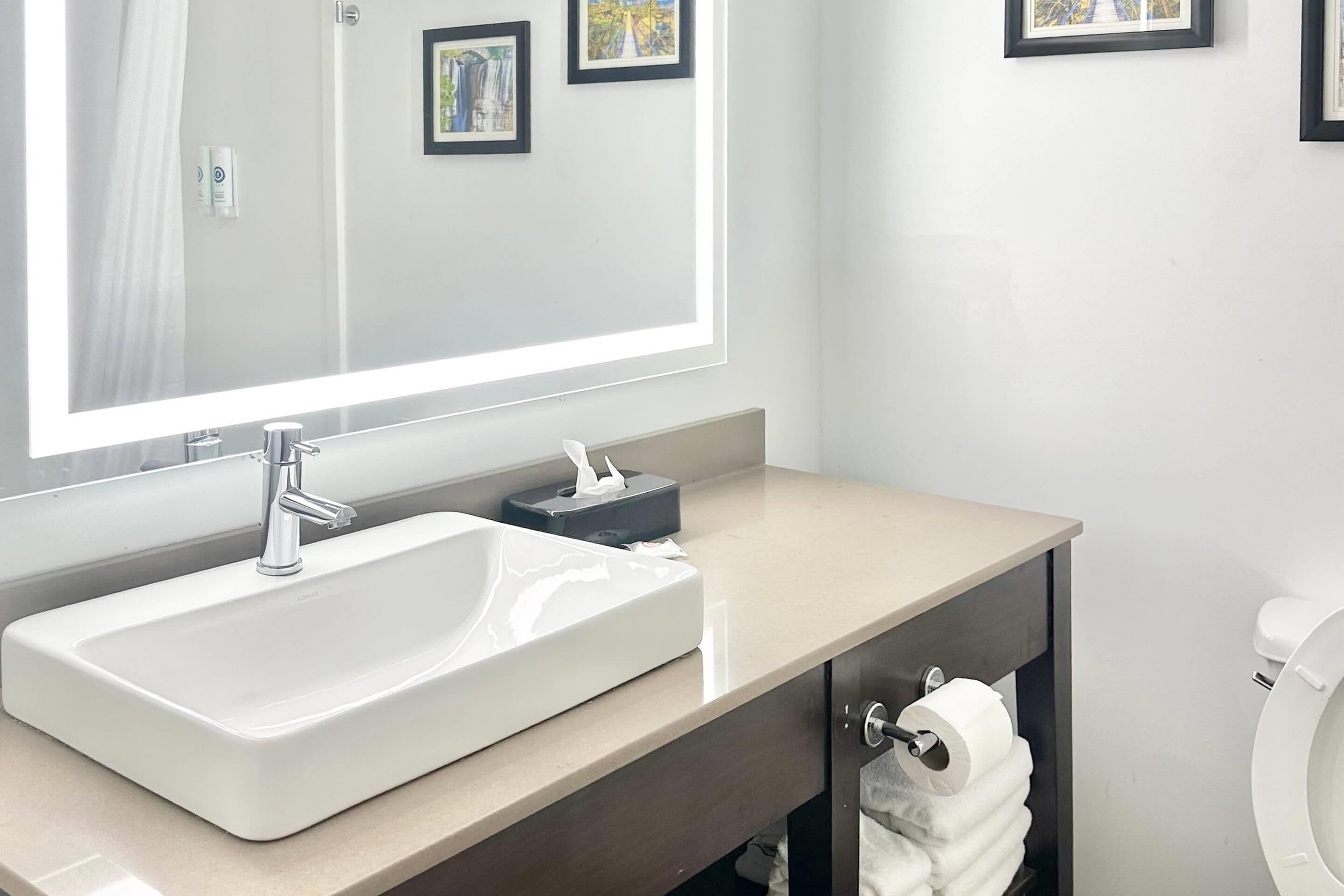 A modern bathroom with a large mirror, a rectangular sink, and a toilet.