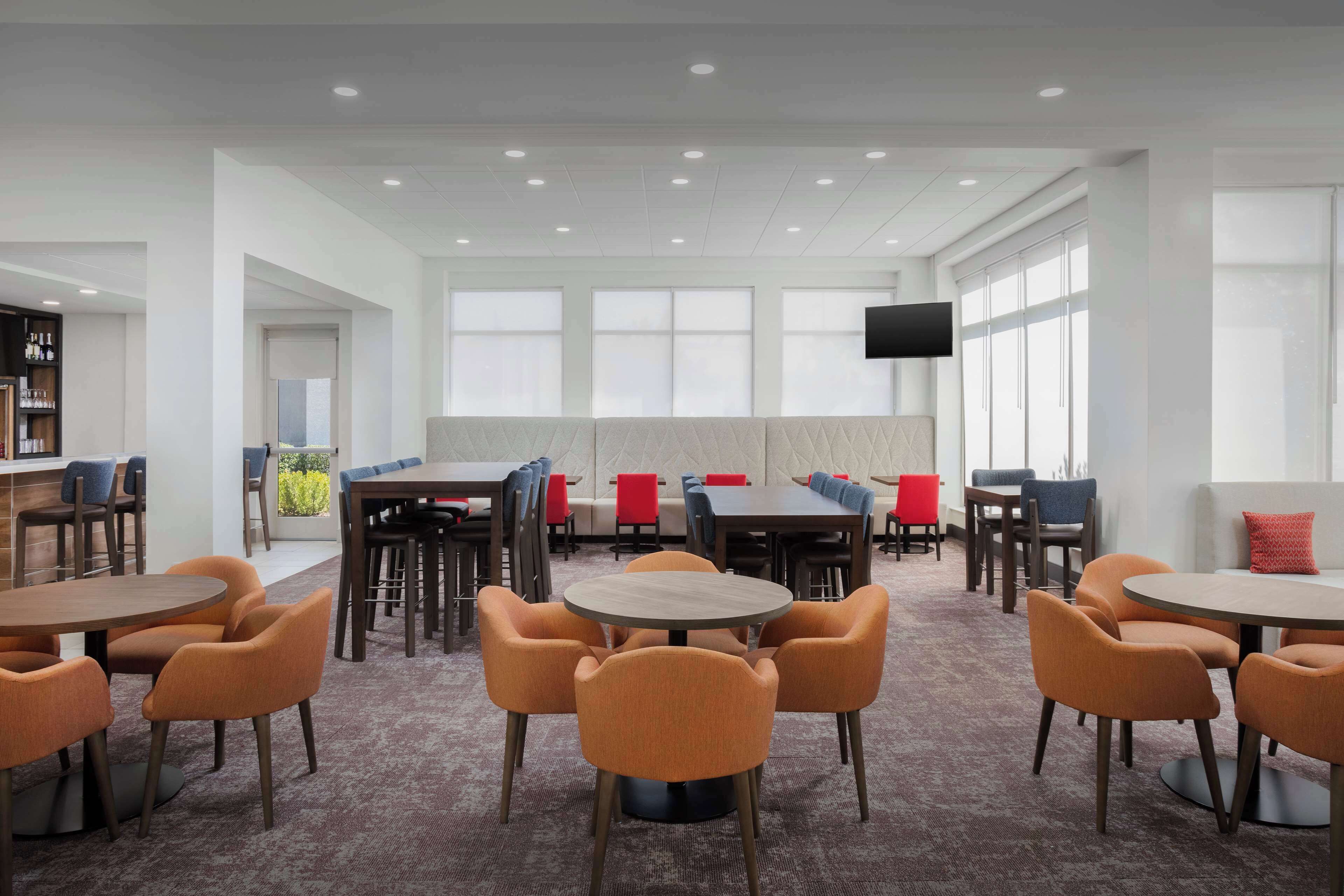 A spacious indoor area with multiple tables and chairs, a flat-screen TV mounted on the wall, and large windows allowing natural light.