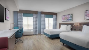 Habitación de hotel con dos camas, un escritorio, una silla y ventanas amplias con cortinas.