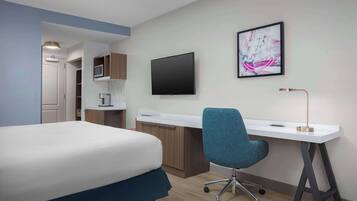 Una habitación de hotel con una cama, un escritorio, una silla, un televisor y un cuadro en la pared.