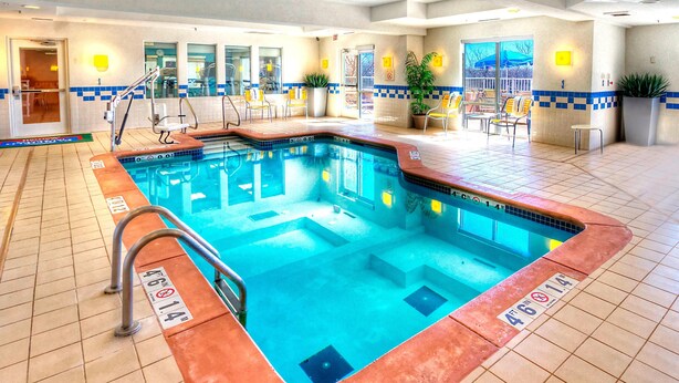 Una piscina interior con suelo de baldosas, una escalera de piscina y una zona de estar con sillas y mesas.
