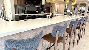 A modern bar area with a long counter, multiple hanging pendant lights, and bar stools.